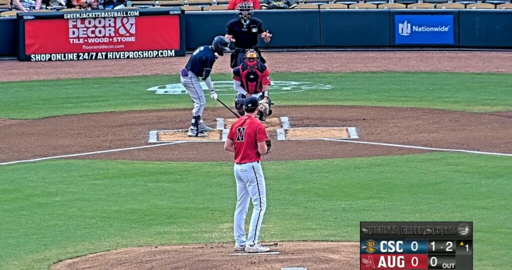 Image capture of a televised Augusta GreenJackets minor league baseball game showing a batter about to swing at a pitch, in front of homeplate signage installed by Van Wagner.